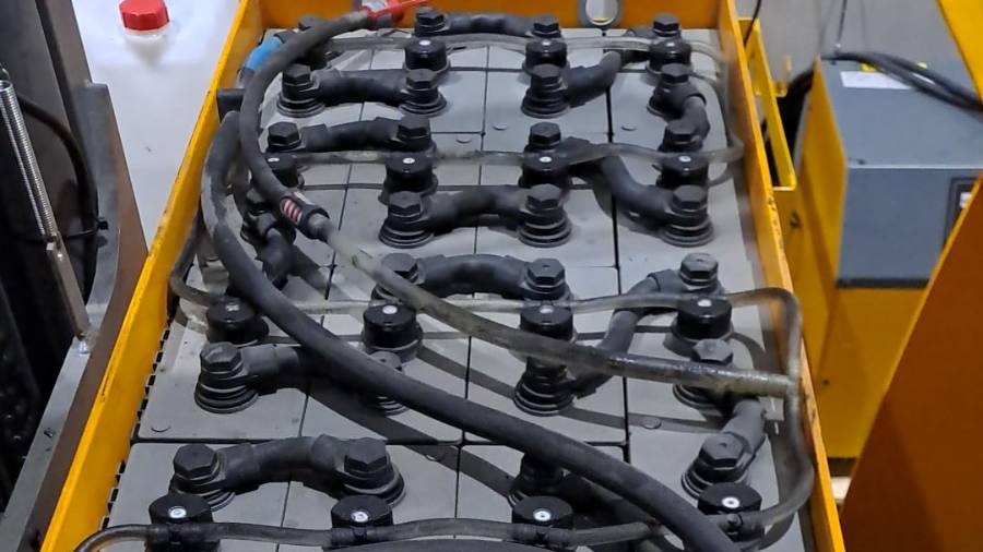 Open lead-acid forklift traction battery showing the cells, vent caps and inter-cell connectors, with the water top-up bottle beside it